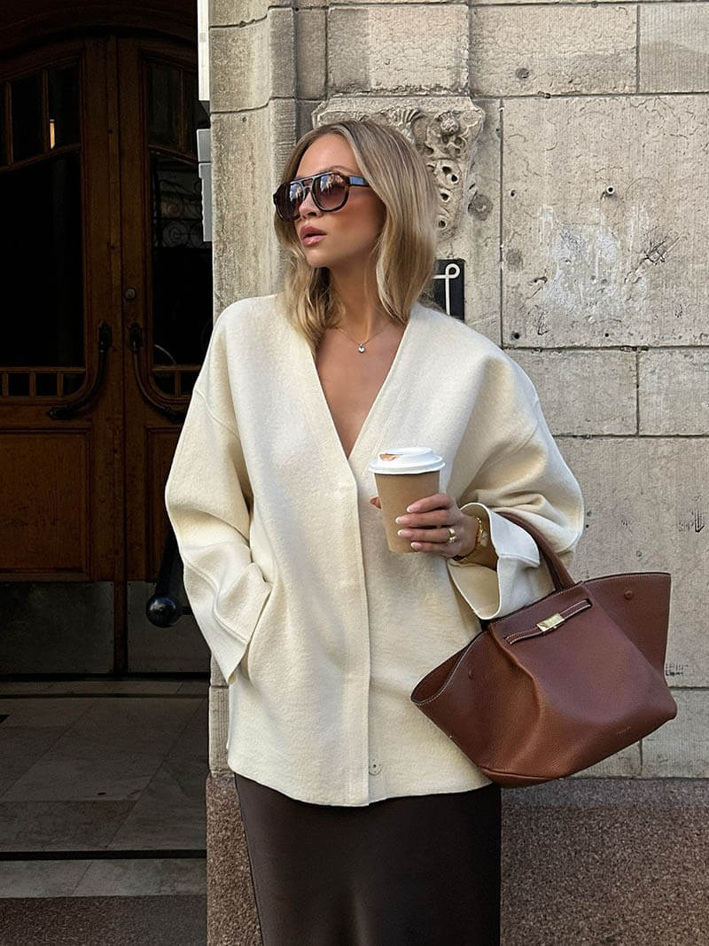 Woman in a cream oversized jacket carrying a brown handbag